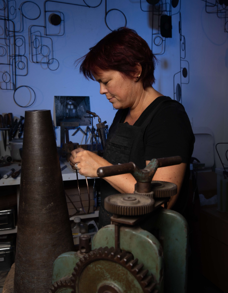 Artist Jacky Oliver sitting in a studio with metal and wire artwork supplies all around her.