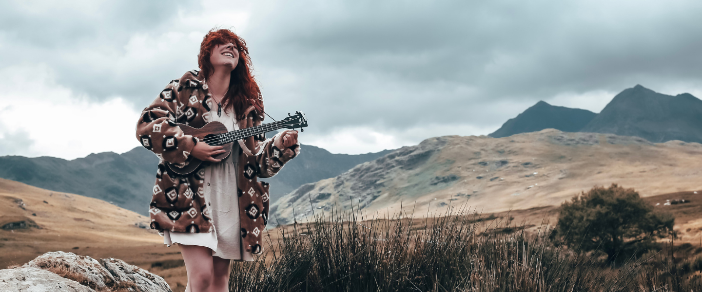 A women holding a ukulele with a back drop of mountains 