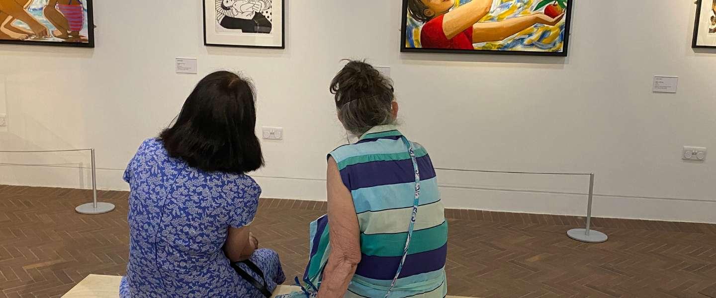 Two people sat looking at art work on a wall